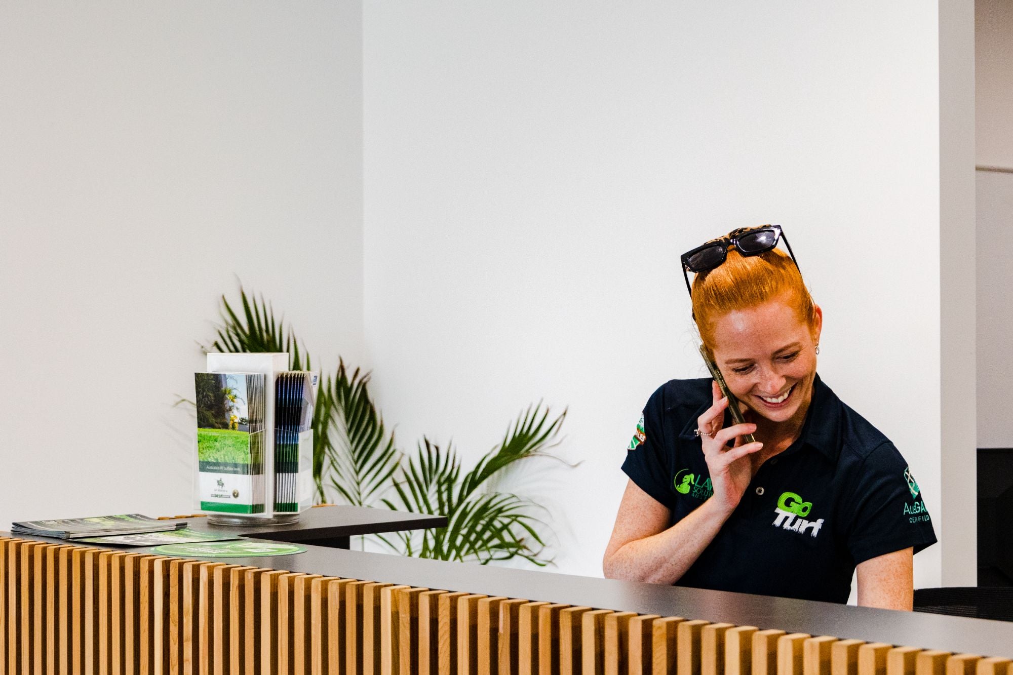 Person in a black shirt with a logo on a phone call at a reception desk.